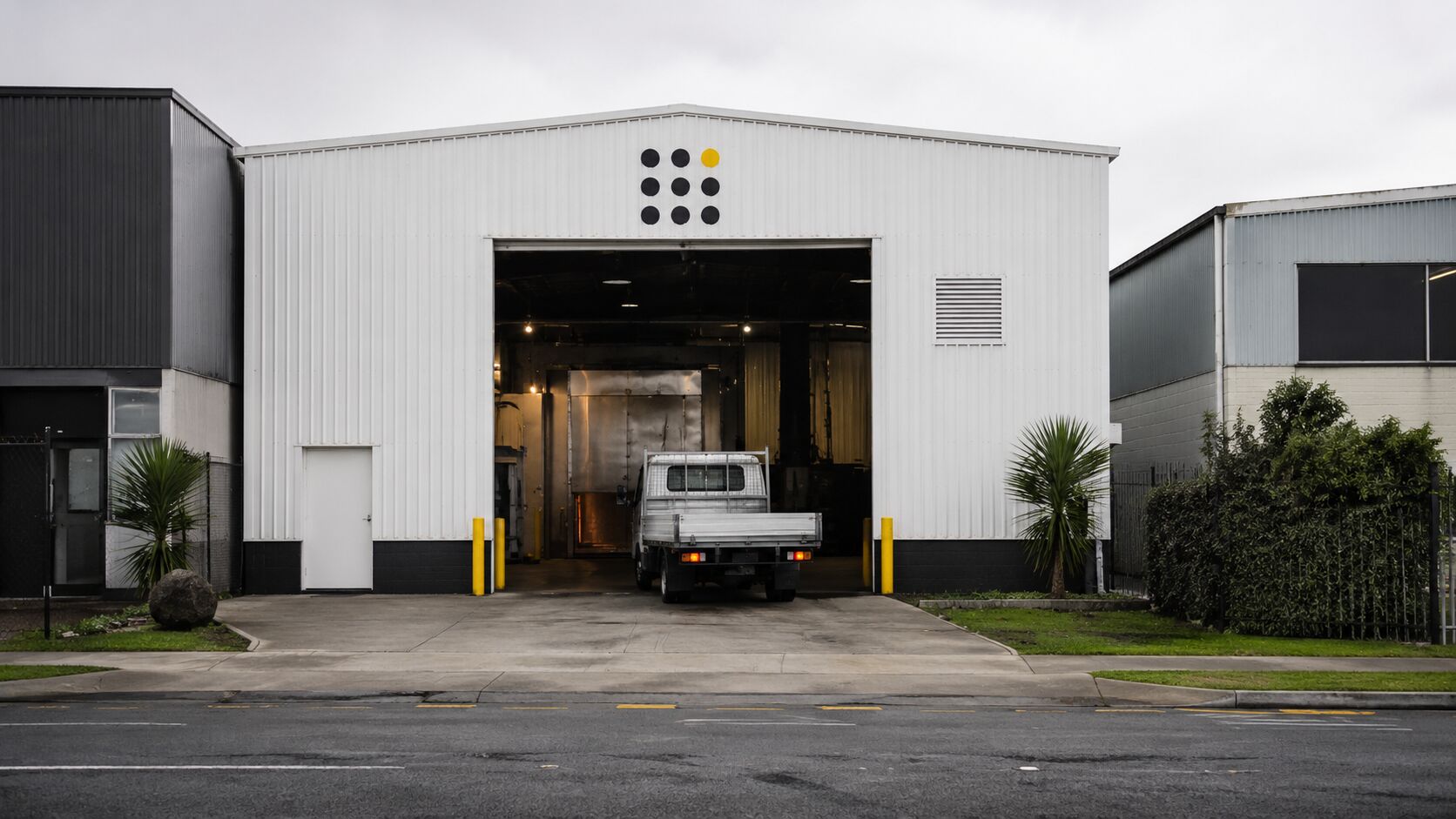 The Bay Powdercoaters workshop on Maleme Street in Greerton, the BPC dot pattern mark above the open roller door, a flatbed reversing in